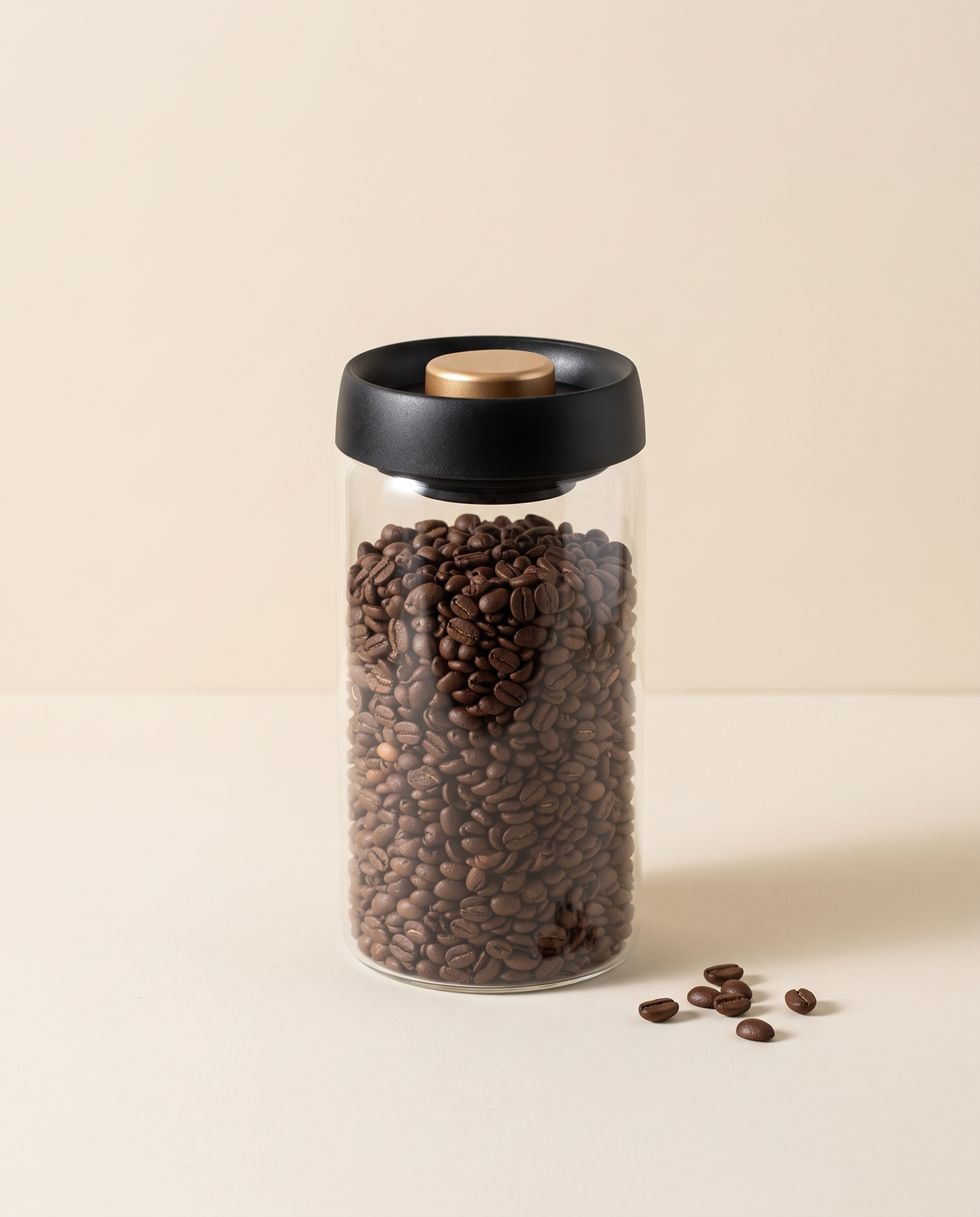Glass vacuum coffee canister with black and gold lid, filled with coffee beans