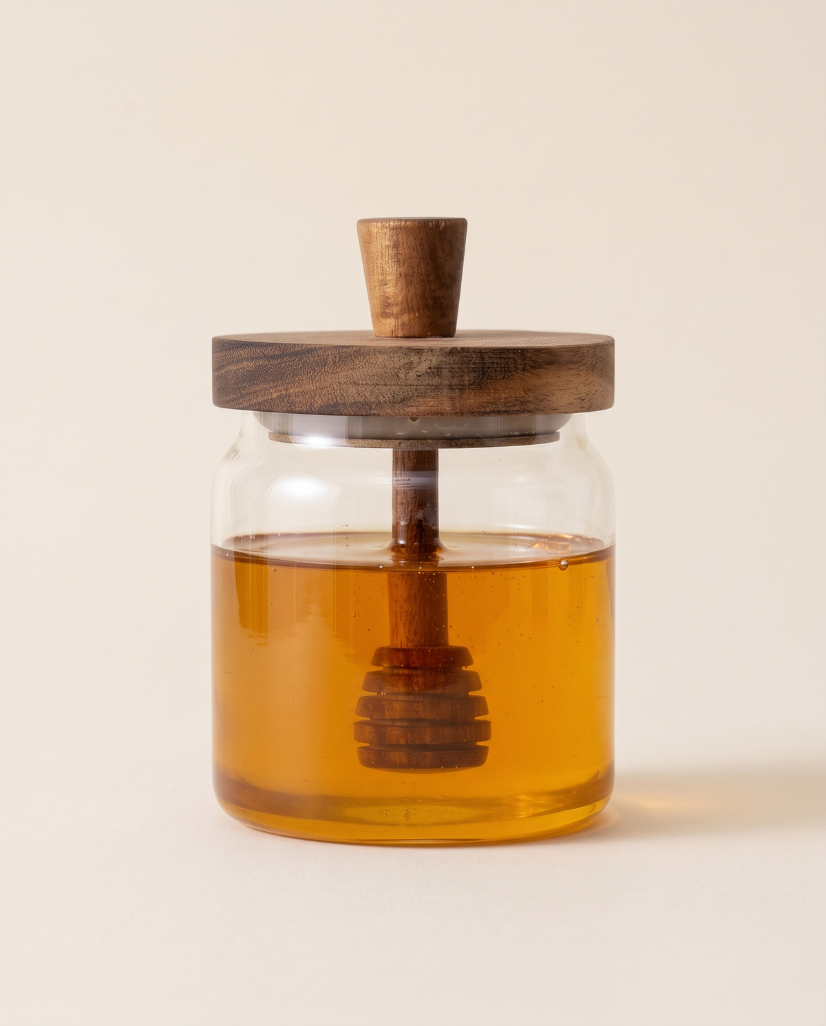 Glass honey jar with acacia lid and dipper, filled with honey