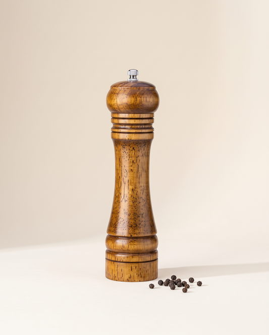 Oak wood pepper grinder with peppercorns on a cream background