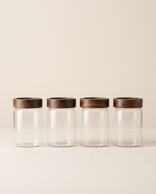 Four glass jars with dark acacia wood lids on a cream background