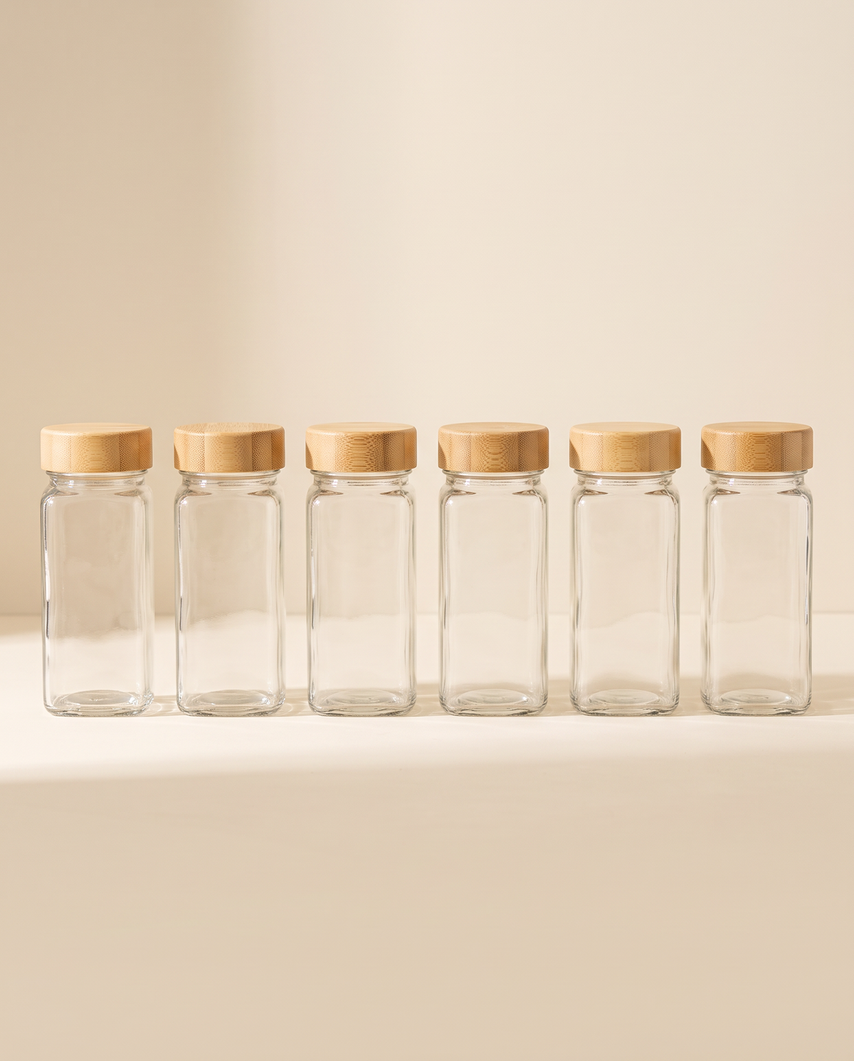Six glass spice jars with bamboo lids on a cream background